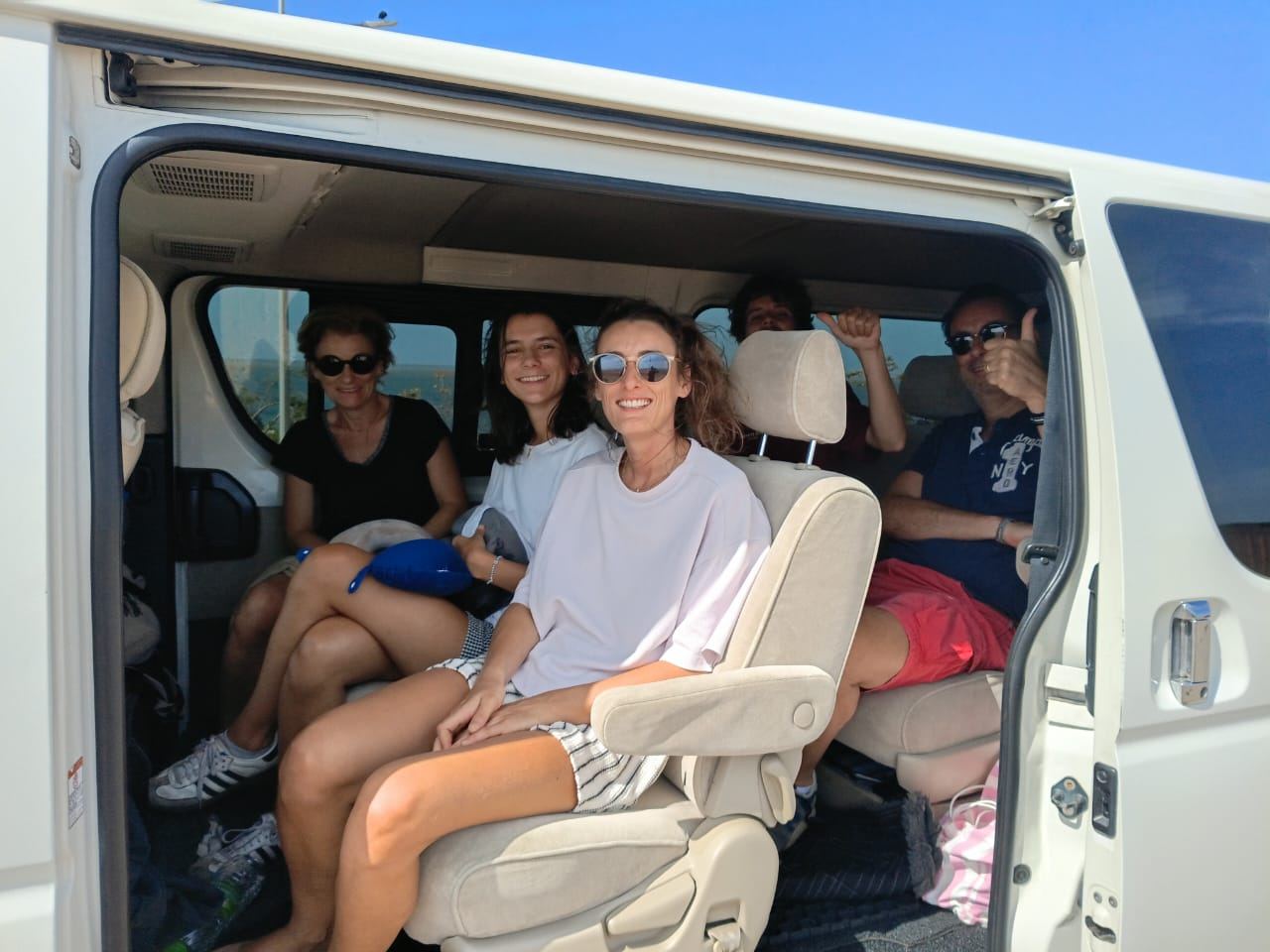 Smiling guests sitting in a Toyota HiAce van with the door open