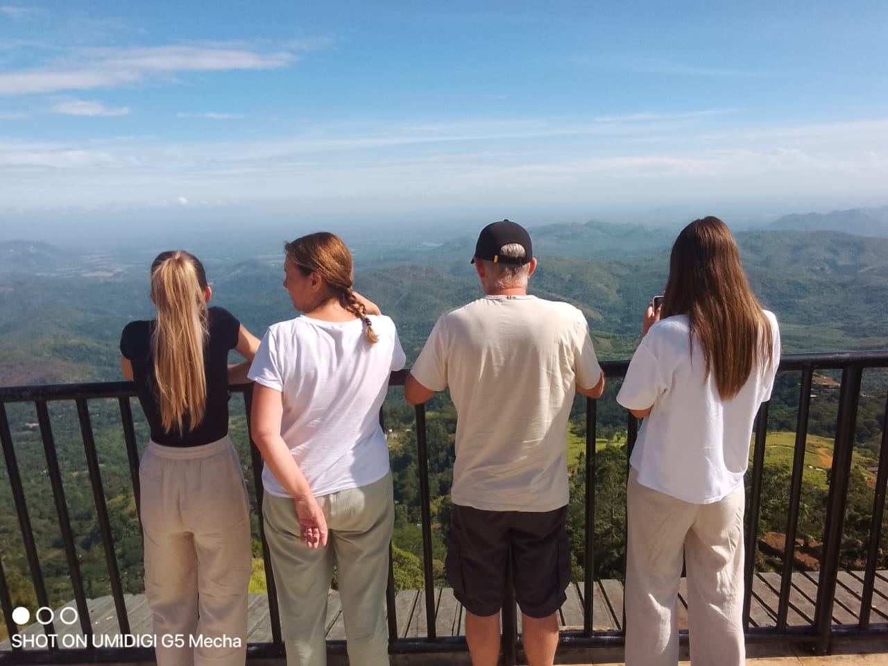 A family looking out over green hills from a viewpoint railing