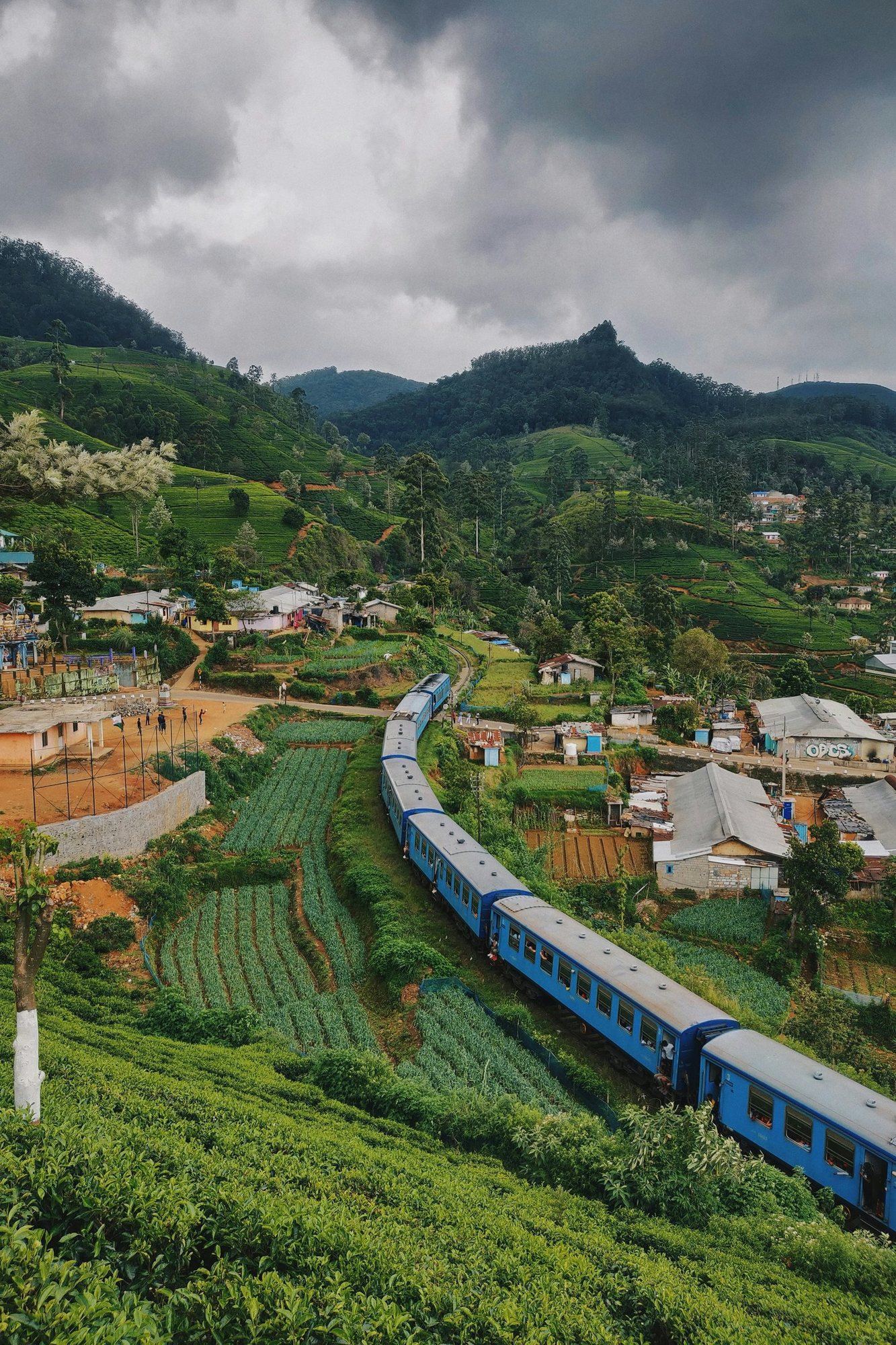 Blue train travelling past houses in the hills